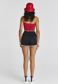 Top corto de rayas rojas, pantalones cortos negros con ribete blanco y un sombrero tipo pescador rojo a juego. El conjunto presenta un diseño ajustado y tela elegante.