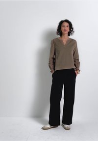 Maglioncino marrone a maniche lunghe con scollatura a V e maniche arricciate, abbinato a pantaloni neri a gamba larga e sneakers bianche. Ambientato su uno sfondo semplice.