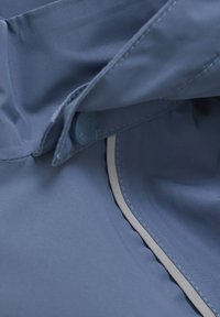 Tissu bleu avec une texture lisse, comportant un bouton et des coutures grises contrastantes le long du bord. Le design détaillé montre une couche pliée.