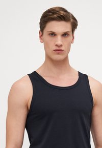 Schwarzes Baumwoll-Tanktop mit runder Ausschnittform, breiten Trägern und glatter Textur, das eine taillierte Passform aufweist.