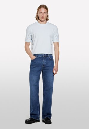 T-shirt bleu clair à manches courtes, coupe décontractée, assorti à un jean droit bleu foncé et des chaussures noires. Style simple et décontracté.