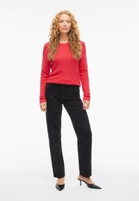 Punainen, teksturoitu neulepusero pitkillä hihoilla, yhdistetty mustiin, leveälahkeisiin samettihousuihin. Malli käyttää mustia, teräväkärkisiä korkokenkiä.