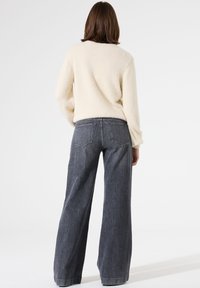 Cremefarbener, flauschiger Pullover mit lockerem Schnitt, kombiniert mit hoch taillierter, dunkelblauer Denim-Weitbein-Jeans mit Kontrastnähten und Gesäßtaschen.