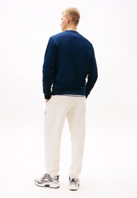 Marine sweatshirt, crèmekleurige sweatpants en sportieve schoenen. De sweatshirt heeft een geribbelde zoom en manchetten, terwijl de broek een relaxte pasvorm heeft met elastische manchetten.
