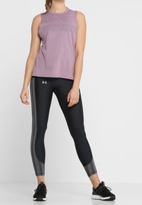 Ljuslila ärmlös topp med textdetalj, matchad med svarta leggings med randig sidopanel och svarta träningsskor.