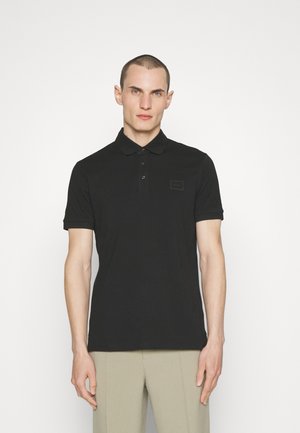 Polo shirt noir en tissu lisse, doté d'une patte de boutonnage à trois boutons, de manches courtes et d'un petit logo brodé sur la poitrine.
