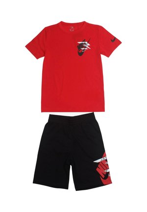 T-shirt rossa a maniche corte con logo Nike nero e bianco e pantaloncini neri con grafica Nike rossa e bianca sulla gamba sinistra.