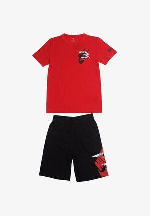 T-shirt rossa a maniche corte con logo Nike nero e bianco e pantaloncini neri con grafica Nike rossa e bianca sulla gamba sinistra.