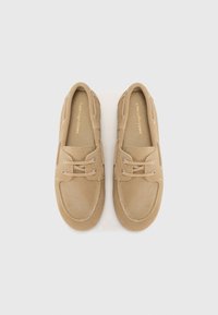 Beige Wildlederschuhe mit einer runden Zehenform, zwei Ösen für die Schnürsenkel und gestickten Details um die Sohle. Flache Sohlen für die Freizeit.