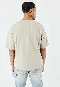 Camiseta de gran tamaño de color beige con un diseño de contorno de cactus en la parte de atrás, mangas cortas y un corte holgado. Combinada con unos pantalones vaqueros de color azul claro.