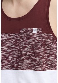 Burgunderfarbendes, ärmelloses Tanktop mit strukturiertem Muster. Verfügt über eine Brusttasche und einen einfarbigen weißen unteren Abschnitt. Etikett auf der Tasche sichtbar.