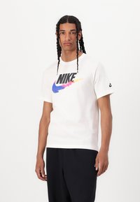 Balta medvilnė t-shirt su dideliu daugiaspalviu Nike logotipu priekyje. Trumpos rankovės ir apvalus iškirpimas. Juodas akcentas ant rankovės.