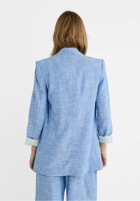 Lichtblauwe linnen blazer met een relaxte pasvorm, notched lapels en opgerolde mouwen met gestreepte manchetten. Soepele textuur met een subtiele glans.
