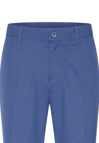 Siniset kudotut housut, joissa on tasainen etuosa, nappikiinnitys ja hienovaraiset ompeluyksityiskohdat. Housuissa on taskut ja sileä pinta.