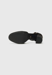 Svarta högklackade sandaler med en texturerad gummisula, ett brett tånstrap och ett smalt vristband med en guldspännedetalj.