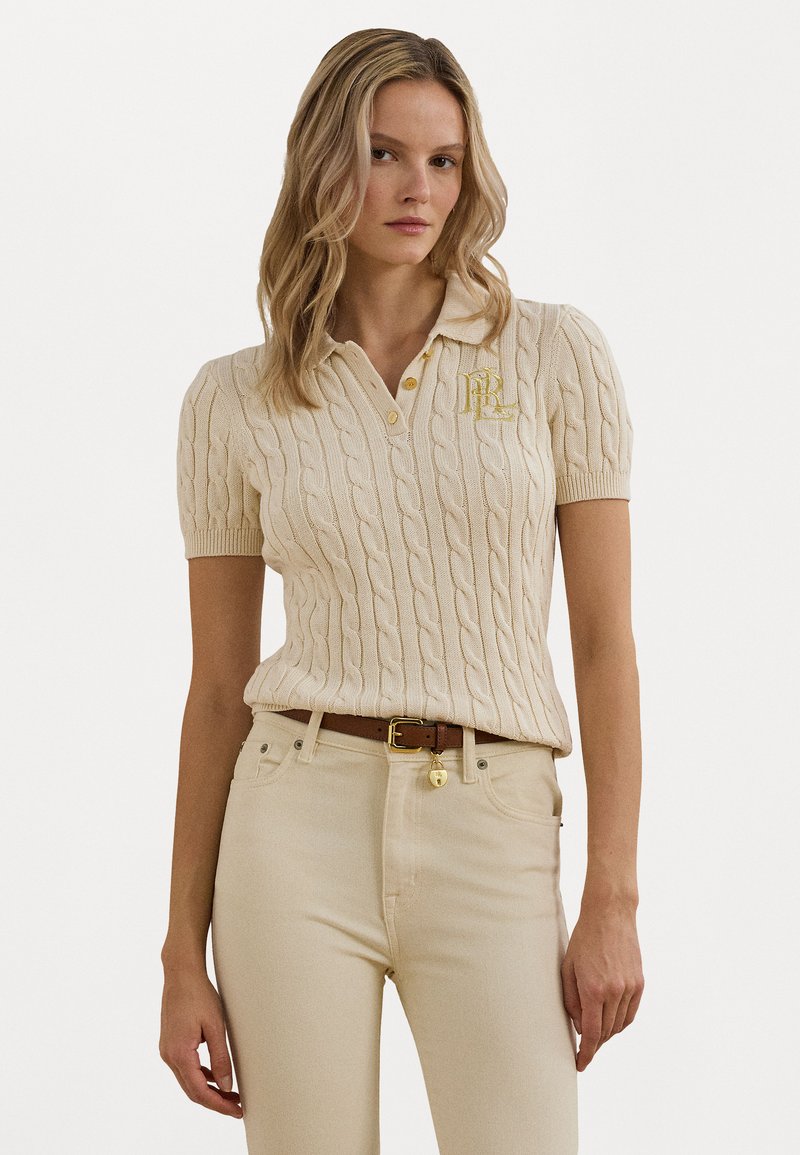 Polo en maille beige avec un motif en maille torsadée, manches courtes, col et logo doré sur la poitrine. Assorti à un jean beige taille haute.
