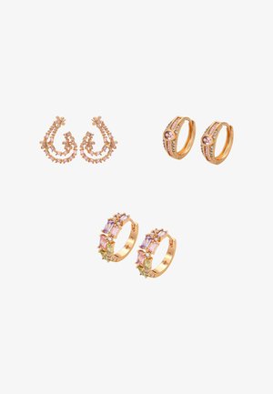 Drie paar gouden creolen met roze, paarse en groene edelstenen, gerangschikt in bloemmotieven en geometrische patronen op een witte achtergrond.