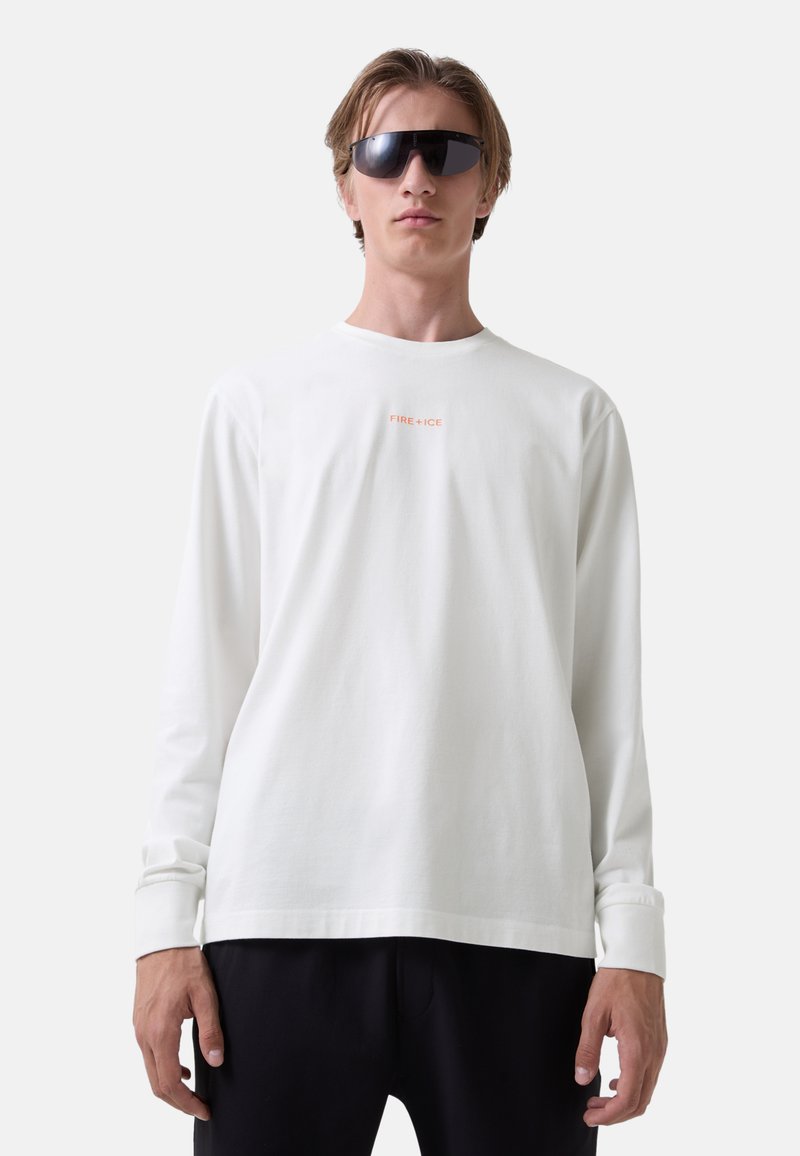 Long-sleeve white shirt in soft fabric with a round neck. Features "FIRE+ICE" orange text on the chest and relaxed fit. Black sunglasses worn.