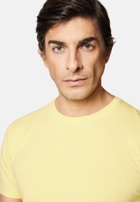 Żółta koszulka z okrągłym dekoltem, wykonana z miękkiej bawełny. Dopasowany krój, krótkie rękawy, gładka faktura i minimalistyczny design.
