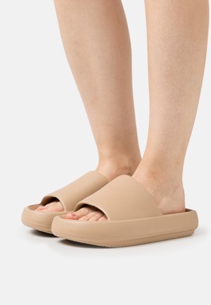 Sandales en caoutchouc beige avec une tige texturée, un design à bout ouvert et une semelle épaisse. Les chaussures présentent une finition lisse et des motifs subtils.