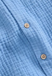 Tela azul texturizada con un patrón de cuadrícula, que presenta un botón beige con cuatro agujeros, un pliegue vertical central y una textura suave y tejida.