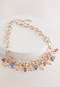 Gold-tone metal necklace with large links and multiple small pendants featuring blue and red stones, showcasing a smooth, polished finish.
