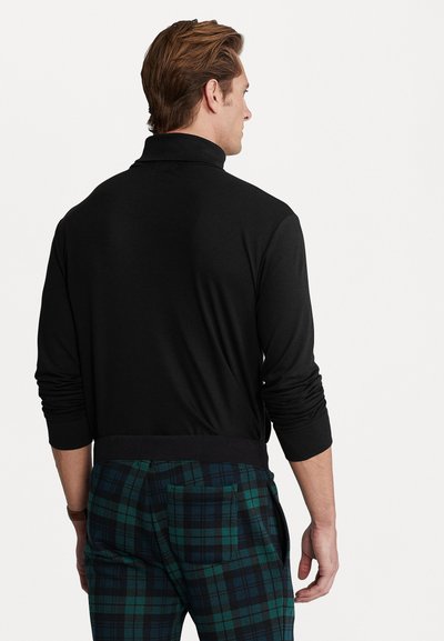 Camisa de polo negra de manga larga con cuello alto. Textura suave. Combinada con pantalones de cuadros en verde oscuro y azul marino que tienen un bolsillo trasero.
