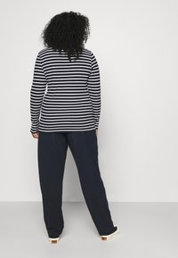 Gestreepte lange mouwen top in marineblauw en wit, gecombineerd met loszittende marineblauwe broeken. Het materiaal lijkt zacht; het ontwerp is casual en comfortabel.