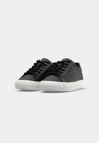 Sneakers nere con motivo testurizzato sui lati, tomaia liscia, punte tonde e suole in gomma bianca. Presentano lacci neri e un design minimalista.