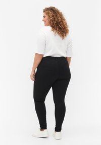 Svarta stretchiga leggings med två bakfickor, parat med en vit topp. Outfiten fulländas med vita sneakers, sedd bakifrån.