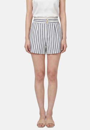 Woman wearing high-waisted white shorts with vertical navy stripes, two front buttons, a white sleeveless top, and beige slide sandals.