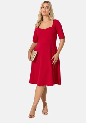 Vestido rojo en línea A con mangas cortas, escote cuadrado, cuerpo ajustado y falda acampanada. Combinado con un clutch dorado y tacones plateados con tiras.