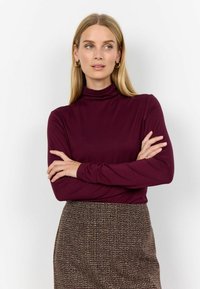 Bordo dugi rukav turtleneck s krojem koji se prilagođava tijelu, u kombinaciji s smešim suknjom s tekstiranim uzorkom. Glatka tkanina s minimalnim detaljima.