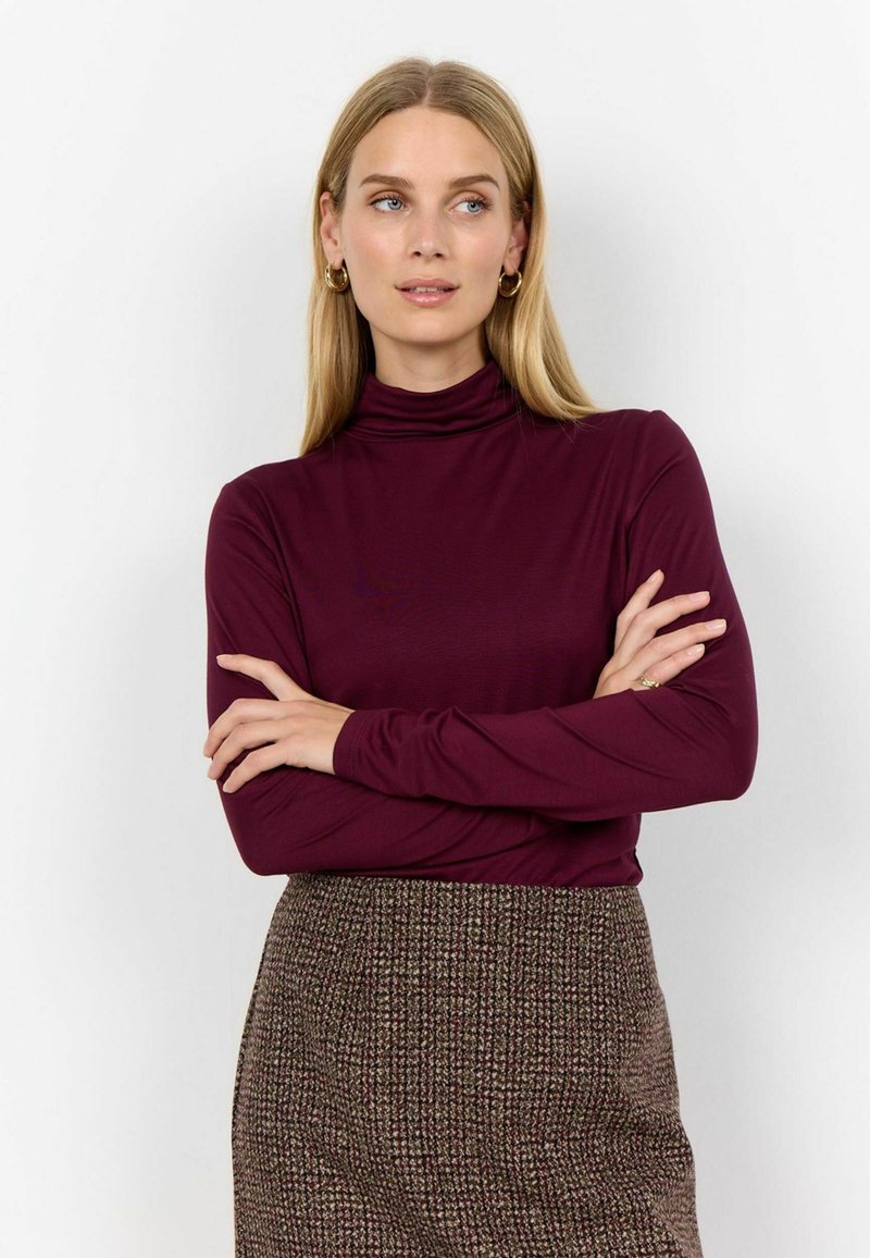 Bordo dugi rukav turtleneck s krojem koji se prilagođava tijelu, u kombinaciji s smešim suknjom s tekstiranim uzorkom. Glatka tkanina s minimalnim detaljima.