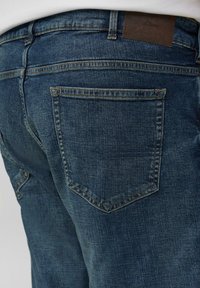 Dunkelblaue Jeans mit strukturierter Oberfläche. Verfügt über klassische Gesäßtaschen und ein braunes Etikett mit geprägt, eingestanztem Markennamen am Bund.