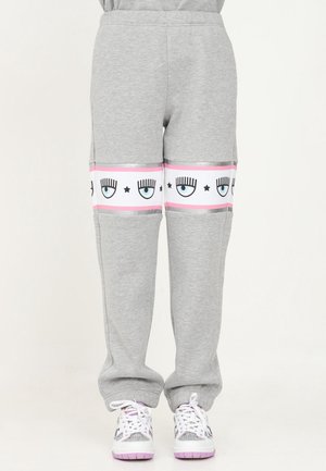 Pantalon de jogging gris avec des bandes blanches et roses autour des genoux, décoré d'yeux bleus avec cils et d'étoiles noires, assorti à des baskets blanches et roses.