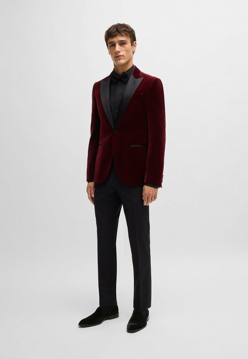 Blazer in velluto bordeaux con revers e dettagli in satin nero, abbinato a una camicia nera e pantaloni neri su misura, completato da mocassini neri.