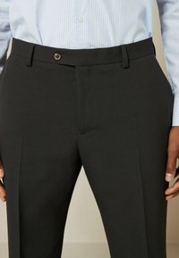 Pantalon noir ajusté en tissu lisse, avec une fermeture éclair et un bouton à l'avant, des poches latérales et un design sans ornements.