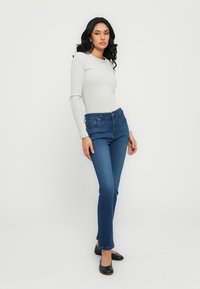 Lichtgrijze lange mouwen top gecombineerd met donkerblauwe skinny jeans. De jeans hebben een klassiek vijf-pocket ontwerp en een lichte flare aan de onderkant.