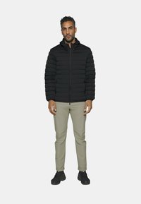 Giacca a vento nera imbottita con design trapuntato orizzontale, chiusura con zip e cappuccio. Abbinata a pantaloni beige chiaro e scarpe da ginnastica nere.