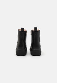 Bottines en cuir noir avec une finition lisse, fermeture éclair latérale et semelle en caoutchouc texturée. Intérieur doublé de fourrure légère.