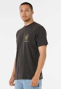 Zwarte katoenen t-shirt met korte mouwen en een ronde hals. Heeft een klein gouden logo op de borst. Gecombineerd met lichtblauwe spijker shorts.