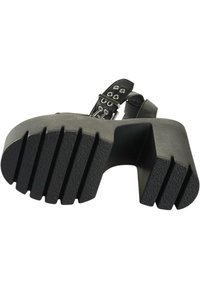 Svart plattformssandal med en texturerad gummisula, som har en bred, böjd klack och flera dekorativa öglor på remmen.