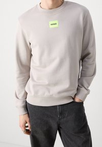 Lichtgrijze sweatshirt met een geribde ronde hals en manchetten, voorzien van een opvallend neon groen rechthoekig label met de tekst "HUGO".