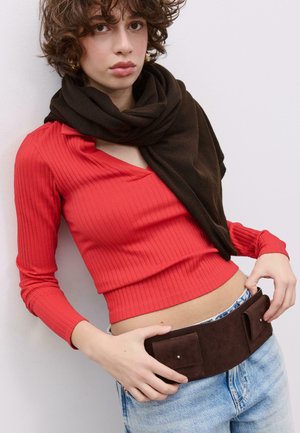 Rdeča rebrasta majica z dolgimi rokavi, kombinirana s temno rjavo ruto. Obleka vključuje širok rjav pas z dvema žepoma, nošen preko svetlo modrih kavbojk.