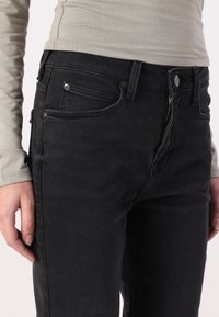 Svarta denimjeans med slim fit, som har framfickor, metalldetaljer och dragkedja. Tyget har en slät, något texturerad yta.
