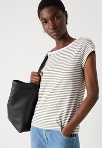 T-shirt a righe con maniche corte, caratterizzata da strisce bianche e verde oliva, abbinata a una borsa a tracolla nera in pelle. Jeans blu in vista.