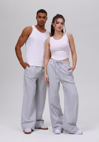 Bela majica na bretele kombinirana s svetlo sivim prugastim širokim pantalonama. Pantalone imaju pojas s vezicom i bočne džepove. Stilizovano s belim patikama.