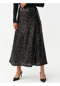 Gonna nera con paillettes e design fluttuante, all'altezza del ginocchio, con una consistenza di tessuto morbida. Indossata con scarpe con tacco nere.