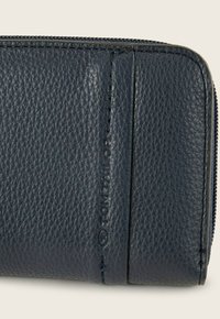 Billetera de cuero azul marino oscuro con un exterior texturizado, que cuenta con un cierre de cremallera y un sutil logotipo en relieve, mostrando detalles de costura ordenados.